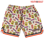 A pair of Halloween youth/adult lifestyle baseball 101 mesh shorts featuring an all-over print of various candy and snack packages on a cream mesh fabric, with orange, black, and white striped trim along the hem. The brand 'SEAMHEAD' is printed on the front.